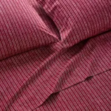 A set of dark red bedding with thin, vertical white stripes, including a flat sheet and pillowcases.