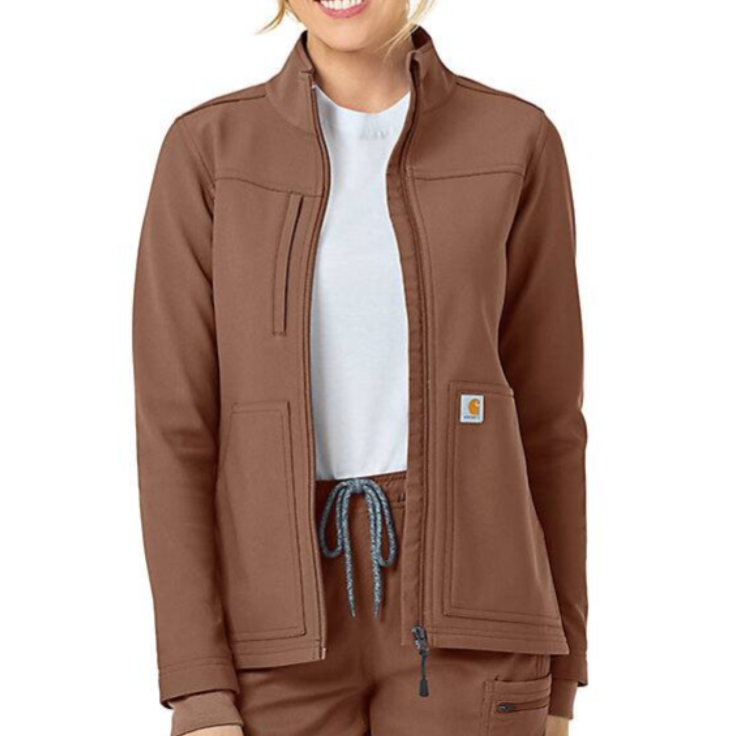 Brown Carhartt Rugged Flex Jacket with a zip-up front, high collar, two large front pockets, and a small Carhartt logo patch on the left pocket. The wearer is styled with matching pants and a white undershirt.