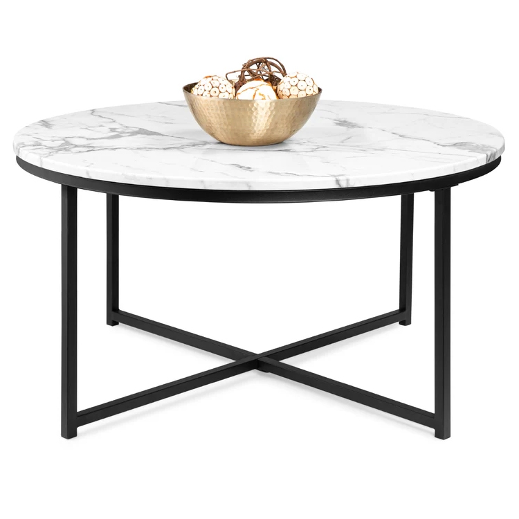 A round coffee table with a faux-marble top and black metal frame, featuring a modern X-shaped base. It holds a gold bowl with decorative orbs.
