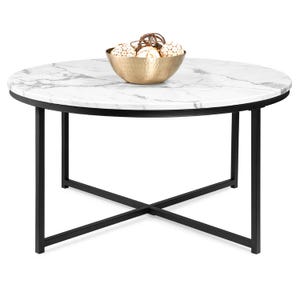 A round coffee table with a faux-marble top and black metal frame, featuring a modern X-shaped base. It holds a gold bowl with decorative orbs.