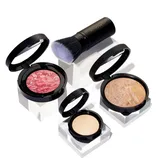 A collection of Laura Geller makeup including a marbled blush, a bronzer with a swirl pattern, a solid compact foundation, and a kabuki brush. The products are displayed on clear stands.