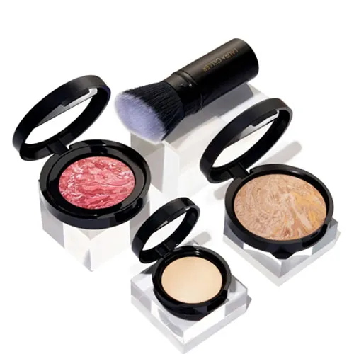 A collection of Laura Geller makeup including a marbled blush, a bronzer with a swirl pattern, a solid compact foundation, and a kabuki brush. The products are displayed on clear stands.