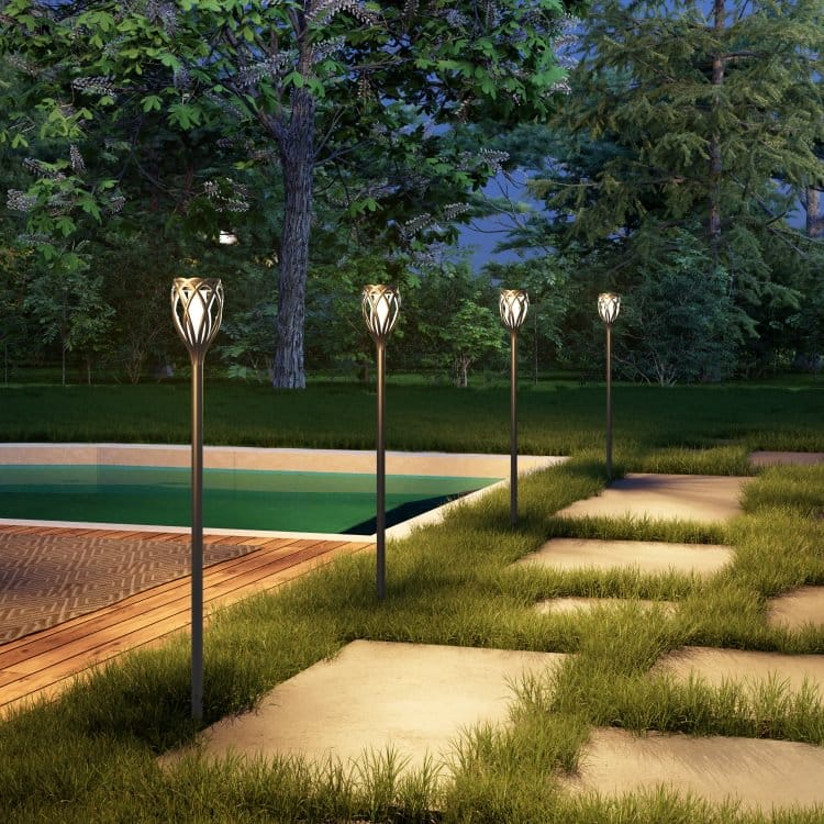 Outdoor path lighting fixtures installed along a walkway near a pool, with decorative floral metal designs, surrounded by grass and trees.