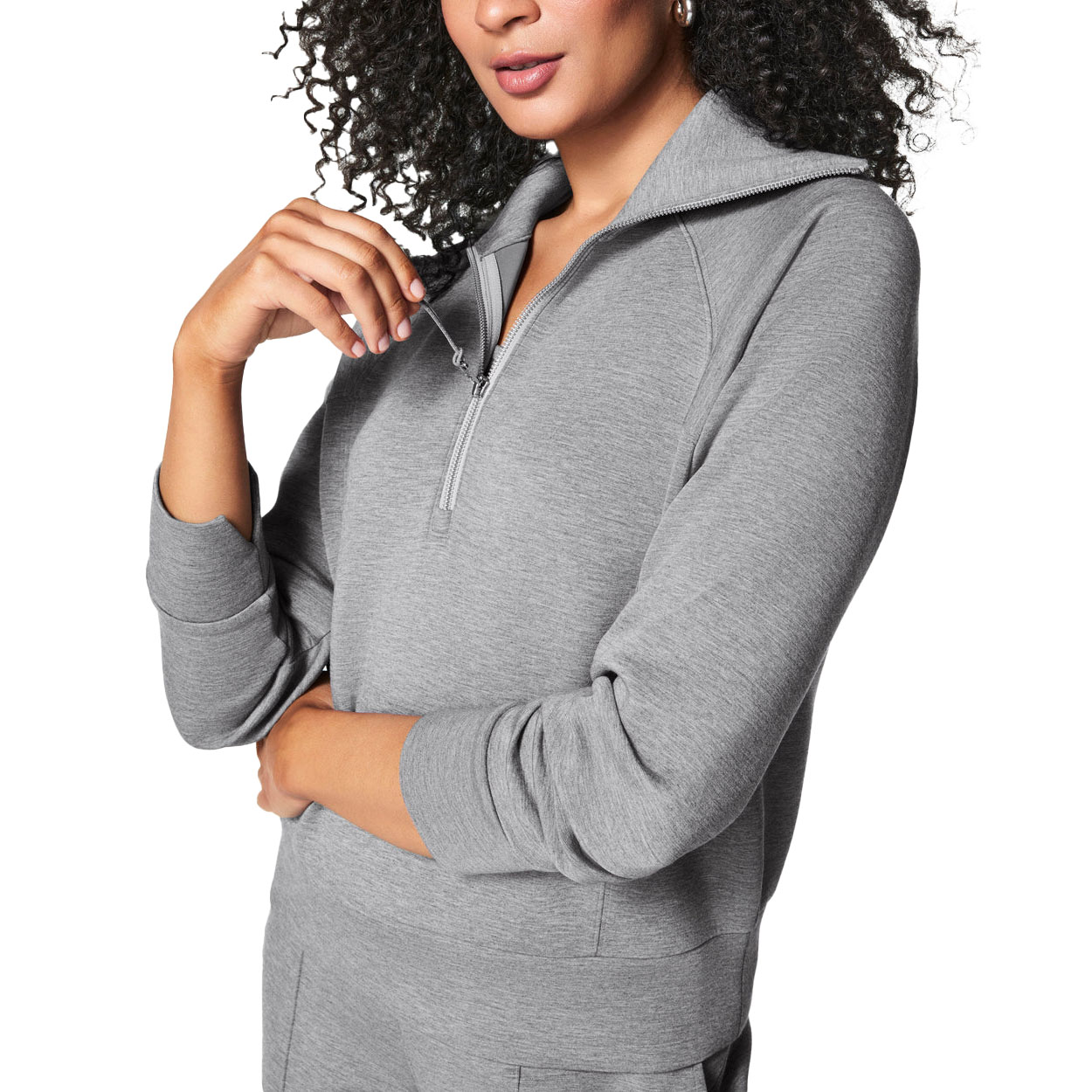 A woman is wearing a grey Spanx AirEssentials Pullover with a half-zip design, long sleeves, and a relaxed fit. The fabric looks soft, and the style is casual and comfortable.