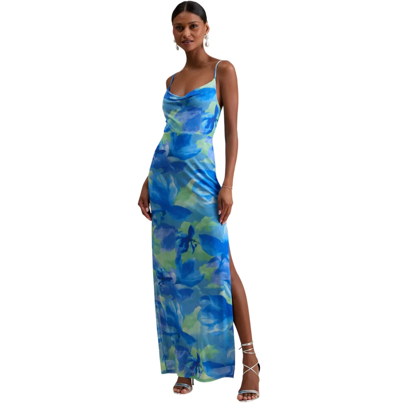 A sleeveless blue and green floral print maxi dress with a cowl neckline, side slit, and thin straps, paired with silver strappy heels and pearl drop earrings.