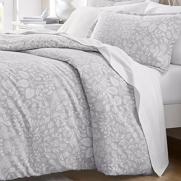A bedding set featuring a duvet cover and pillowcases with a subtle floral pattern in light grey tones, accented with white sheets underneath.