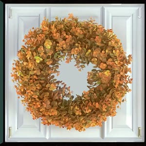 A circular orange and green foliage wreath hanging on a white paneled door.