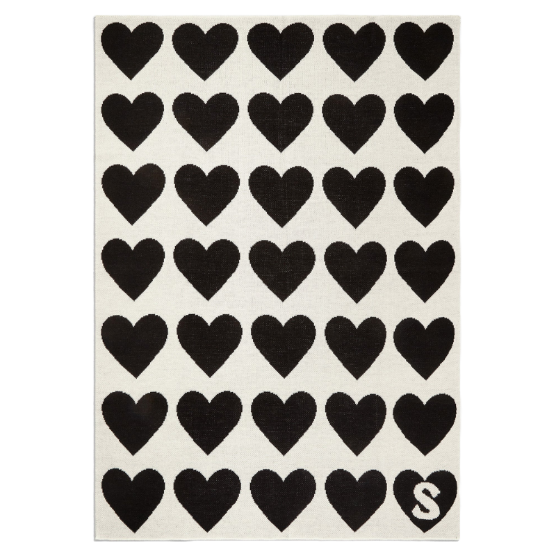 Black heart pattern on a white rectangular rug with the letter \“S\“ in the bottom right corner.