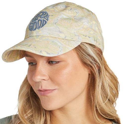 A woman wears a light-colored patterned baseball cap with \“Life is Good\“ embroidered on the front.