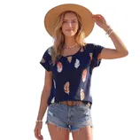 A woman wearing a straw hat, a navy top with a feather pattern, denim shorts, and accessories like a belt, necklace, and bracelets.