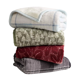 A stack of four cozy blankets with different designs: a white and blue checked pattern, green with tree motifs, red with abstract designs, and a gray plaid.