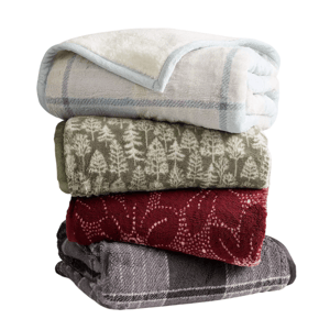 A stack of four cozy blankets with different designs: a white and blue checked pattern, green with tree motifs, red with abstract designs, and a gray plaid.