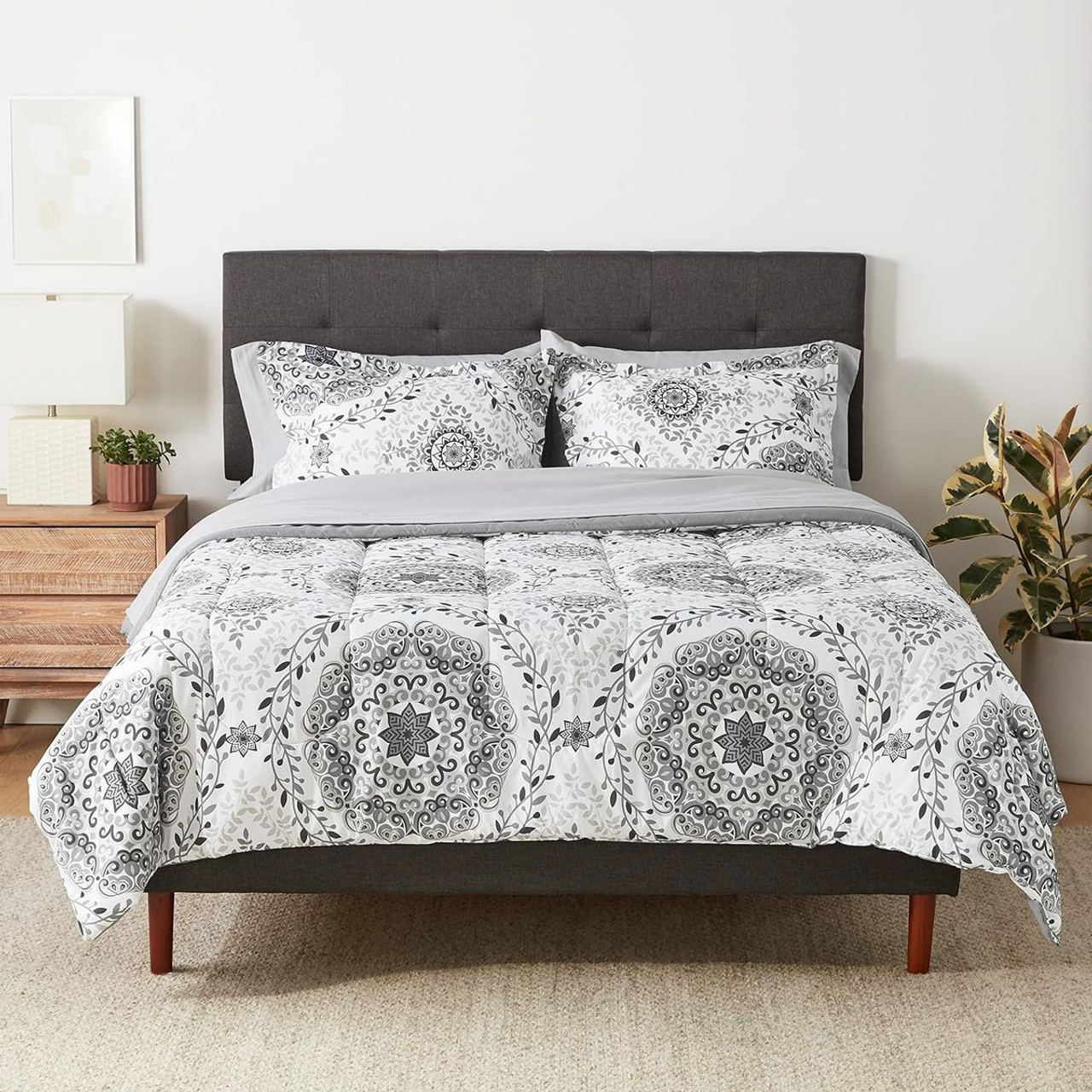 A bed with a gray upholstered headboard and a white and gray patterned bedding set including pillows, sheets, and a comforter.
