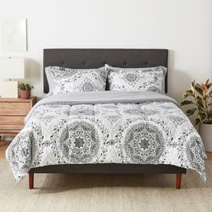 A bed with a gray upholstered headboard and a white and gray patterned bedding set including pillows, sheets, and a comforter.