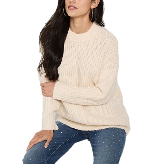 A woman is wearing a cream-colored, knitted sweater paired with blue jeans featuring pearl embellishments.