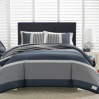 A Nautica Queen Comforter Set with a nautical color palette, featuring wide horizontal stripes in shades of navy, grey, and white, including two matching pillow shams.