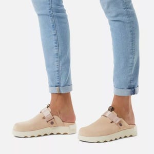 Light beige slip-on shoes with thick white soles and a buckle detail, paired with rolled-up light blue jeans.