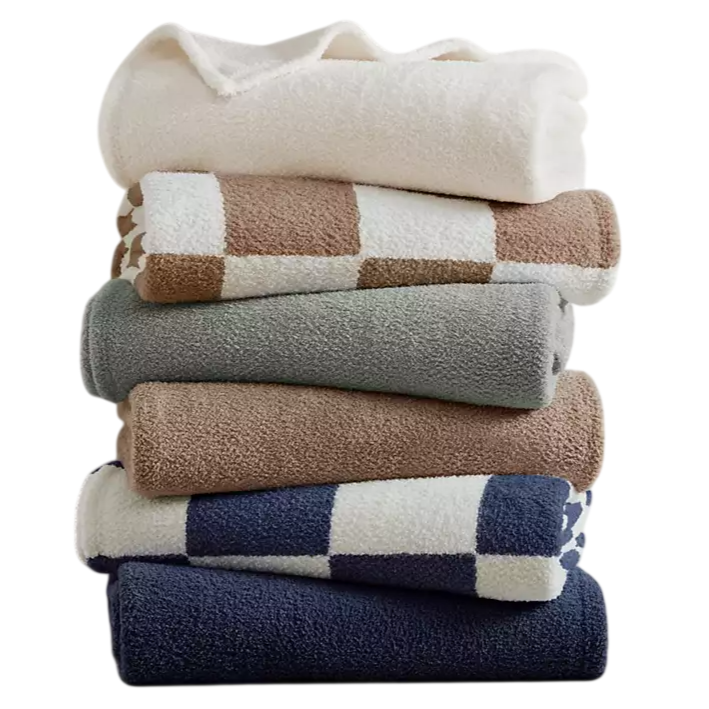 A stack of folded towels in various colors and patterns, including solid white, beige, gray, and blue, with some featuring checkered designs.