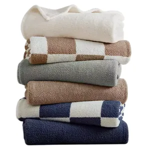 A stack of folded towels in various colors and patterns, including solid white, beige, gray, and blue, with some featuring checkered designs.