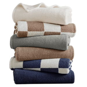 A stack of folded towels in various colors and patterns, including solid white, beige, gray, and blue, with some featuring checkered designs.