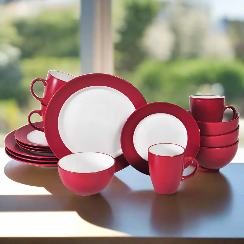 A red and white dinnerware set including plates, bowls, and mugs is displayed on a table, featuring a simple and modern design.