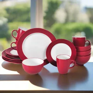 A red and white dinnerware set including plates, bowls, and mugs is displayed on a table, featuring a simple and modern design.