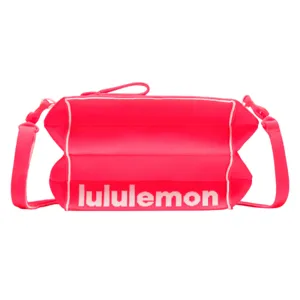 A pink crossbody bag with white piping, featuring the \“lululemon\“ logo in white text across the front.