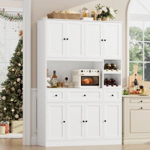 White kitchen pantry featuring multiple cabinets, drawers, a microwave shelf, and wine storage. Decor includes a basket, jars, wine bottles, and floral arrangements. A Christmas tree and gifts are in the background, with a window view of greenery.