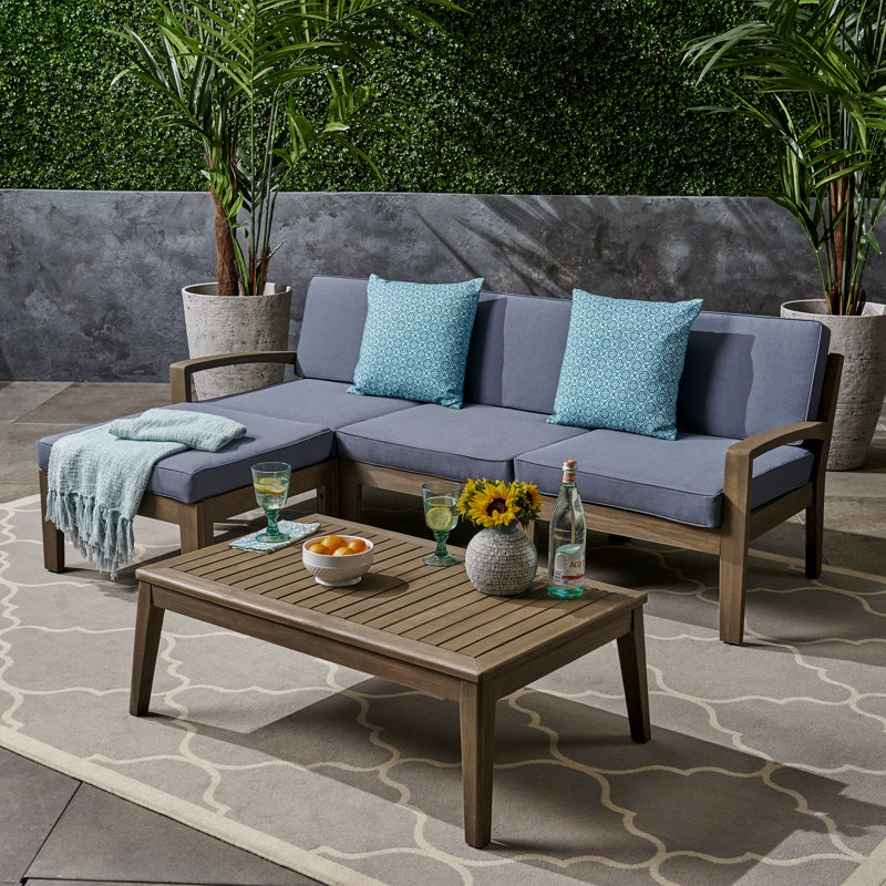 Outdoor furniture set with a sectional sofa, blue cushions, and a wooden coffee table, surrounded by a potted plant and decorative items.