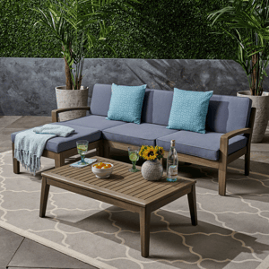Outdoor furniture set with a sectional sofa, blue cushions, and a wooden coffee table, surrounded by a potted plant and decorative items.