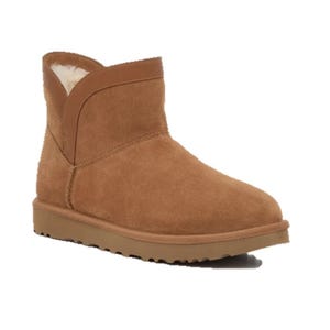 A tan suede ankle boot with a flat sole and soft shearling lining, featuring a short shaft and stitch detailing.