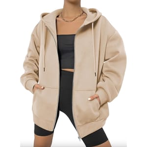 A person wearing a beige oversized zip-up hoodie, black crop top, and black cycling shorts.