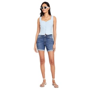 A woman is wearing a light blue sleeveless buttoned top with dark denim shorts, white strappy sandals, and white sunglasses.