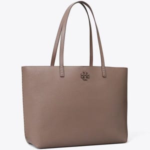 A brown leather tote bag with two handles and a logo on the front.