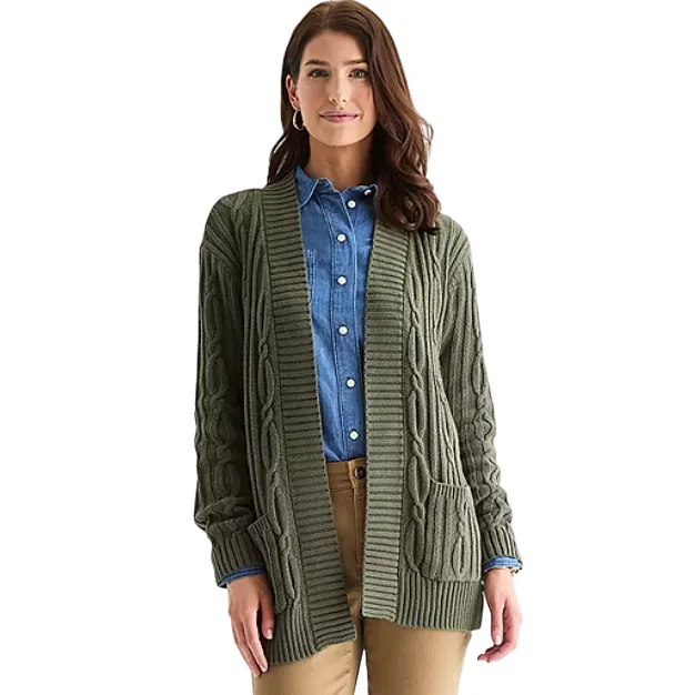 A woman is wearing an olive green cable knit cardigan over a blue denim button-up shirt and beige pants. The cardigan has two front pockets and a ribbed hem.