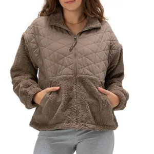 A woman is wearing a taupe, quilted, and faux-shearling jacket with a zipper front and pockets, paired with light gray leggings.