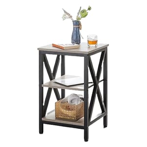 A three-tiered end table with a light-toned wooden top and shelves, supported by a black metal frame, is adorned with a blue vase, a book, and a glass.