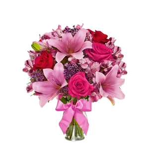 A bouquet featuring pink lilies, pink and red roses, and purple accent flowers, arranged in a clear vase with a pink ribbon.