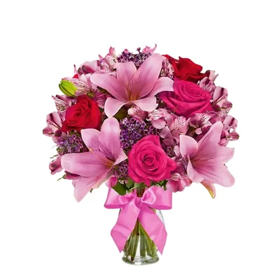 A bouquet featuring pink lilies, pink and red roses, and purple accent flowers, arranged in a clear vase with a pink ribbon.