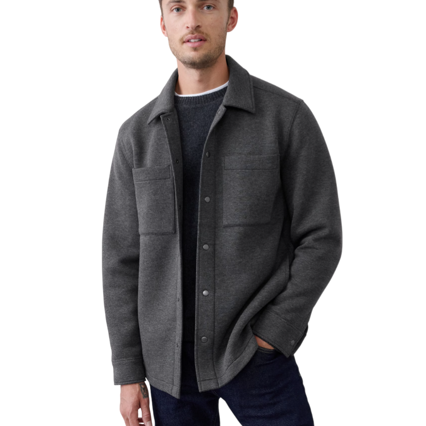 A man is wearing a dark gray wool shirt jacket with snap buttons, featuring two chest pockets, layered over a dark sweater and paired with dark jeans.