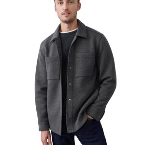 A man is wearing a dark gray wool shirt jacket with snap buttons, featuring two chest pockets, layered over a dark sweater and paired with dark jeans.