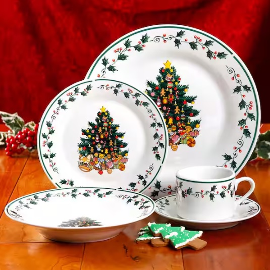 A set of Christmas-themed dinnerware including plates, a cup, and a saucer decorated with a Christmas tree design and holly berry borders.