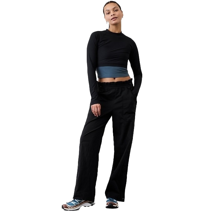A person is wearing a black long-sleeve crop top paired with black wide-leg pants featuring a ruffled waist. They are also wearing sneakers with blue and white accents.