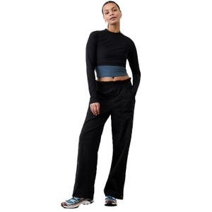 A person is wearing a black long-sleeve crop top paired with black wide-leg pants featuring a ruffled waist. They are also wearing sneakers with blue and white accents.