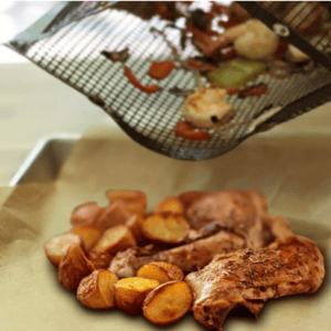 Grilled chicken drumsticks and roasted potatoes on parchment paper, with vegetables being emptied from a woven bag.