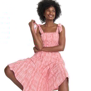 A woman is wearing a Lands' End Textured Tie-Shoulder Dress featuring a red and white vertical stripe pattern. The dress has bow-tied shoulders and a flowy, knee-length skirt.
