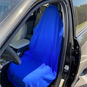 A car interior with a blue cover draped over the driver's seat, partially obscuring it. The car door is open, revealing beige leather seats and a black exterior.