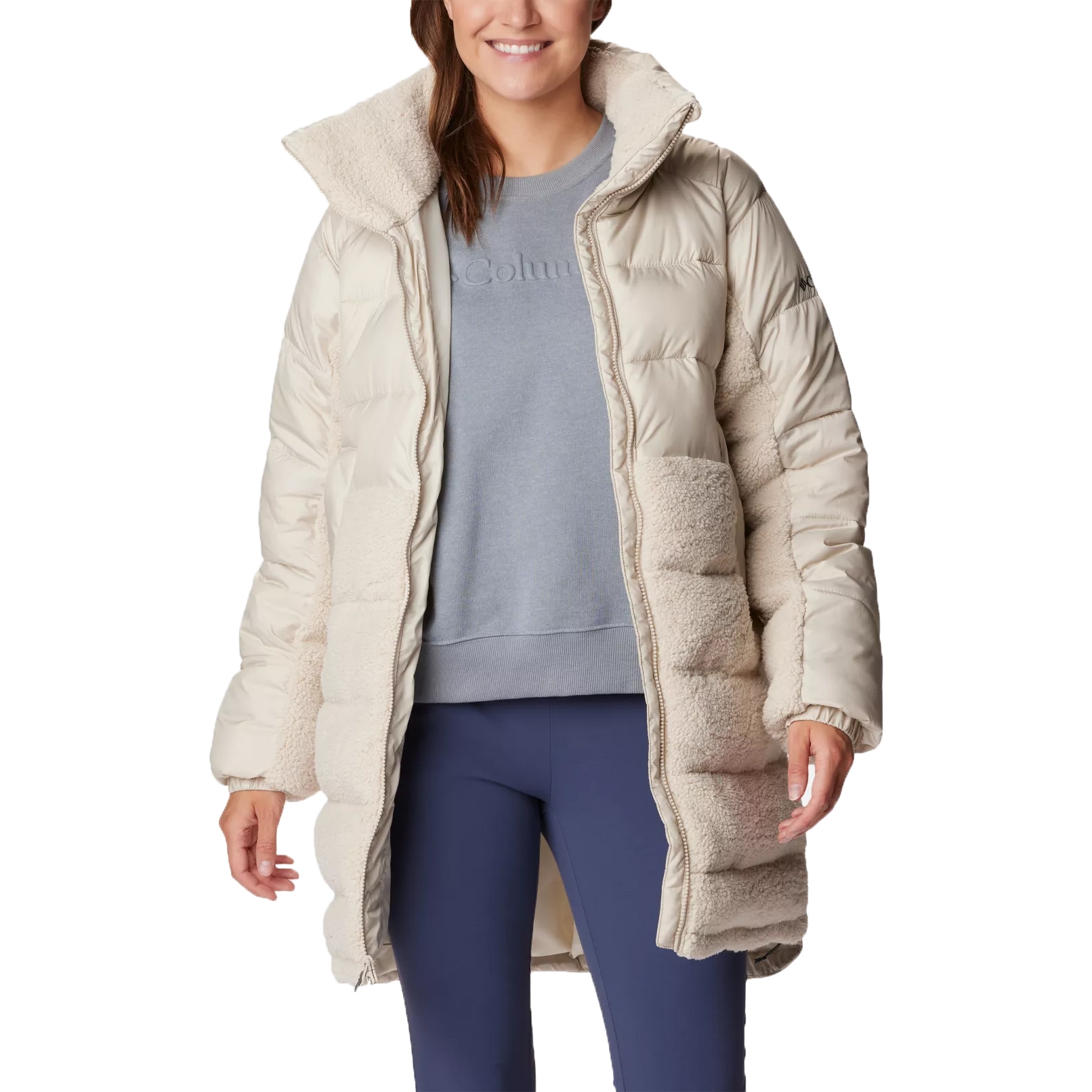 Woman wearing a beige and cream Columbia jacket with a hood, a gray sweatshirt, and blue leggings.