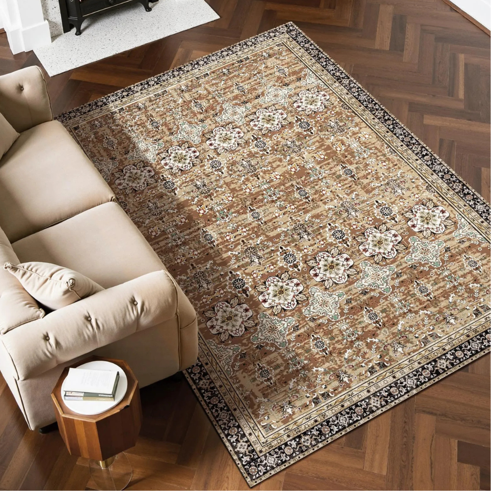 A beige and cream Persian-style area rug with floral and geometric patterns is placed on a herringbone hardwood floor beside a light beige sofa and a small wooden side table.