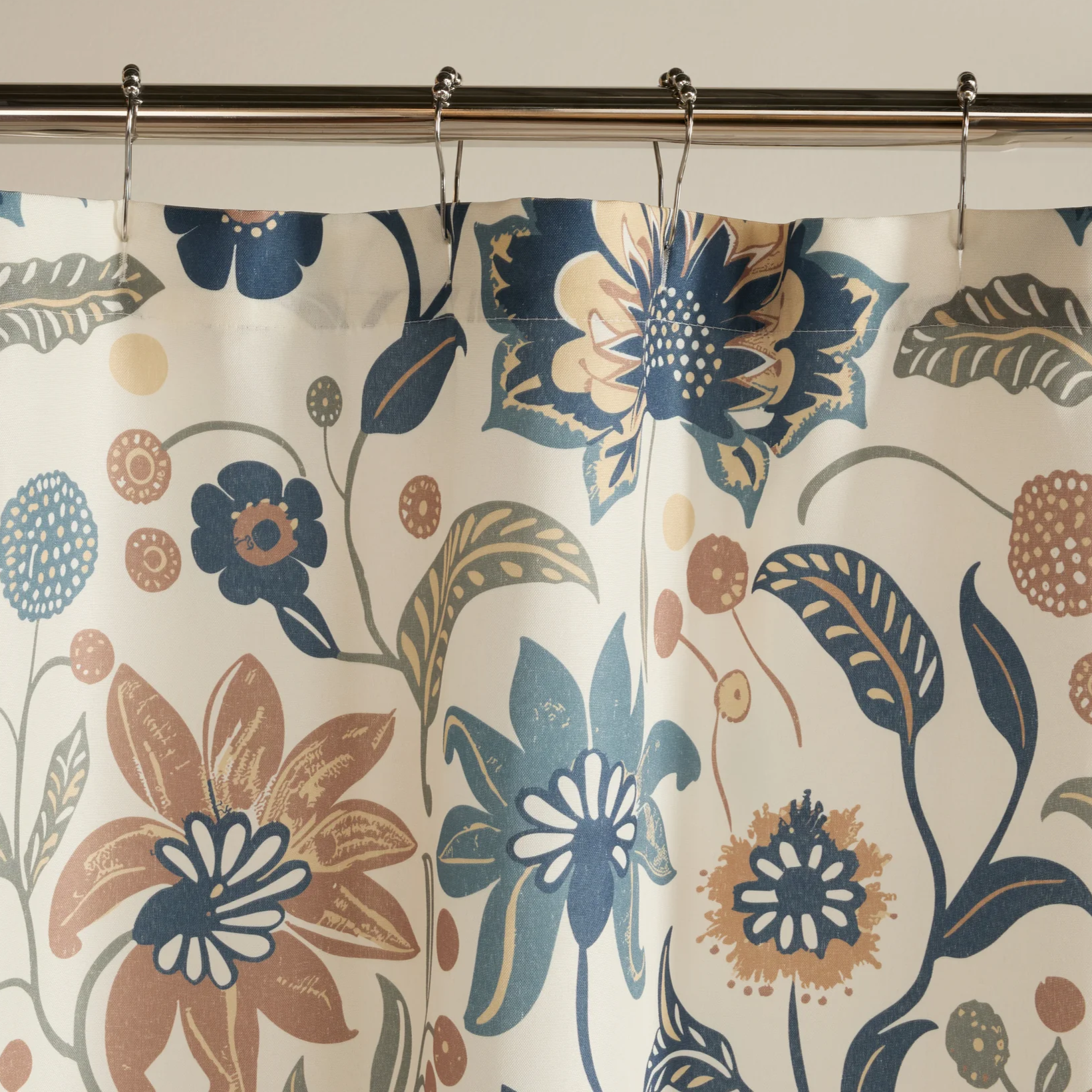 A floral-patterned shower curtain with blue, beige, and brown flowers and leaves hangs from a metal rod with hooks.